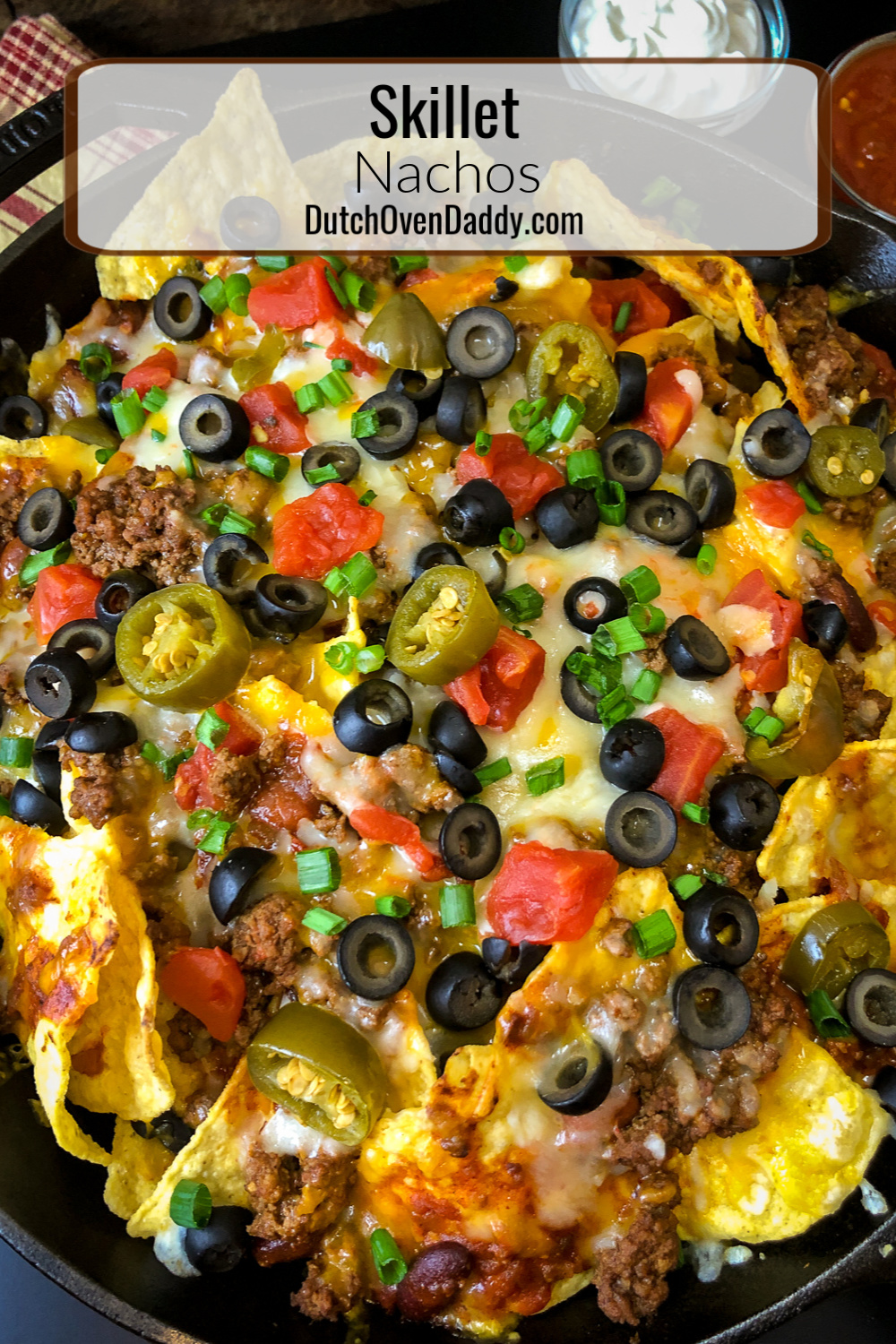 Skillet full of loaded nachos with sour cream and salsa in the background. 