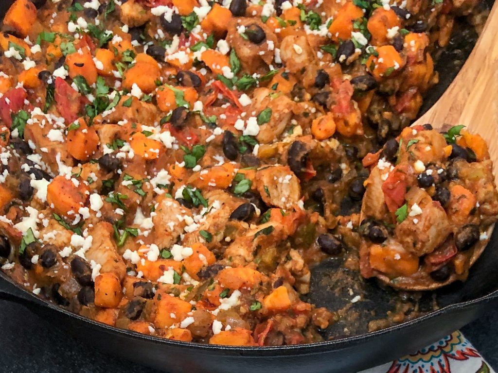 Close up shot of the Mexican inspired skillet dinner with a wooden spoonful of the dish. 