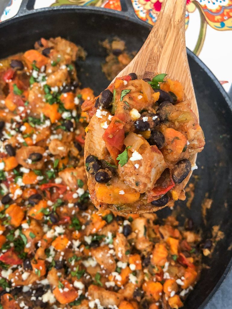 A wooden spoon serving the skillet dinner that has been garnished with fresh cilantro and queso fresco. 