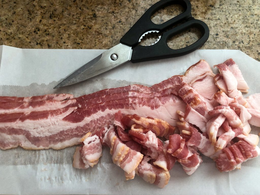 Strips of bacon on parchment paper, with some cute pieces and kitchen shears. 