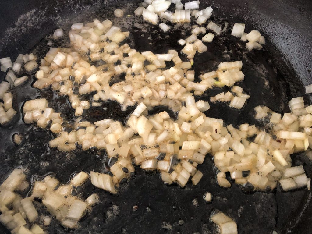 Diced onions sautéing in bacon fat in a cast iron skillet. 