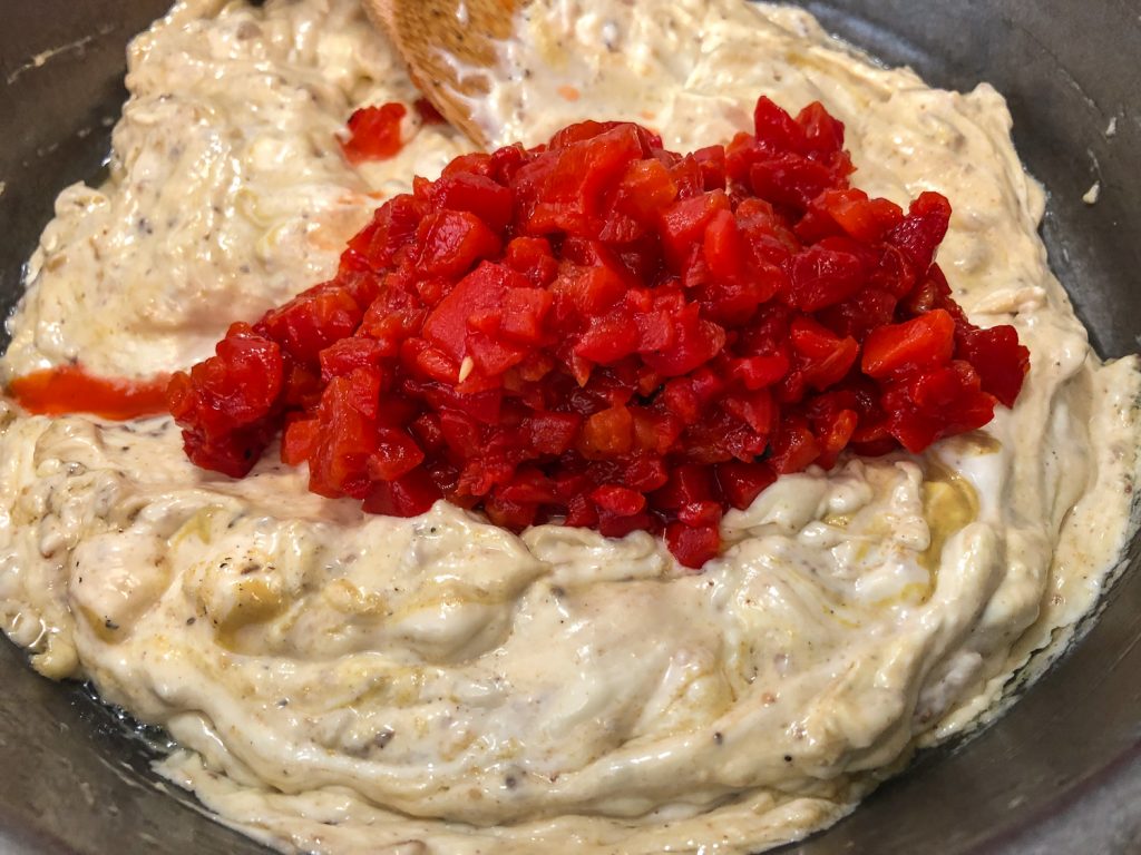Chopped roasted red peppers being added to the creamy dip mixture. 