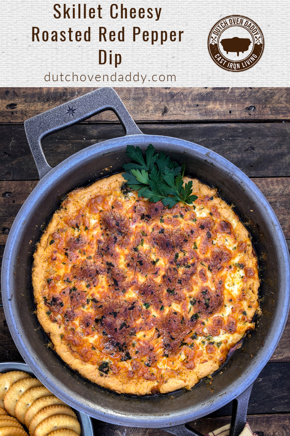 Branded image of Cheese and Roasted Red Pepper dip in a cast iron skillet with a plate of crackers at the bottom. 