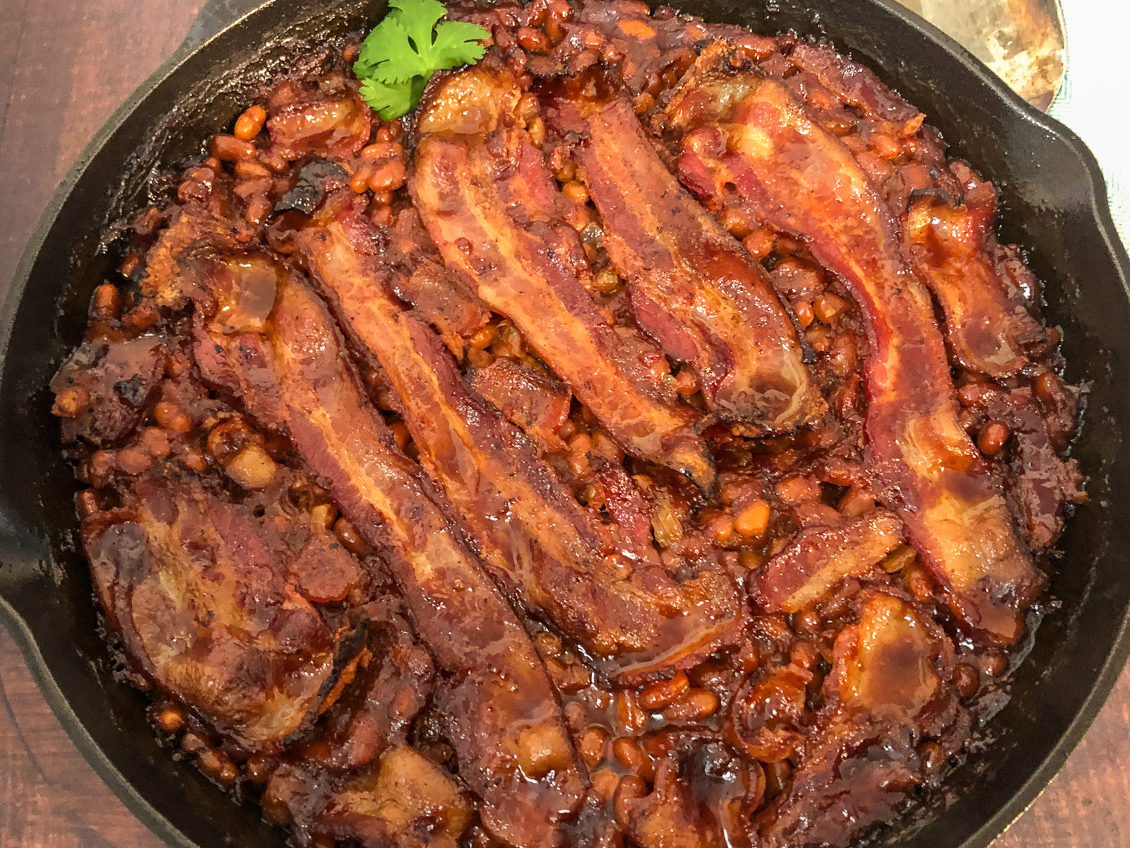 Close up of finished baked beans with bacon showing caramelized sauce and crispy bacon strips