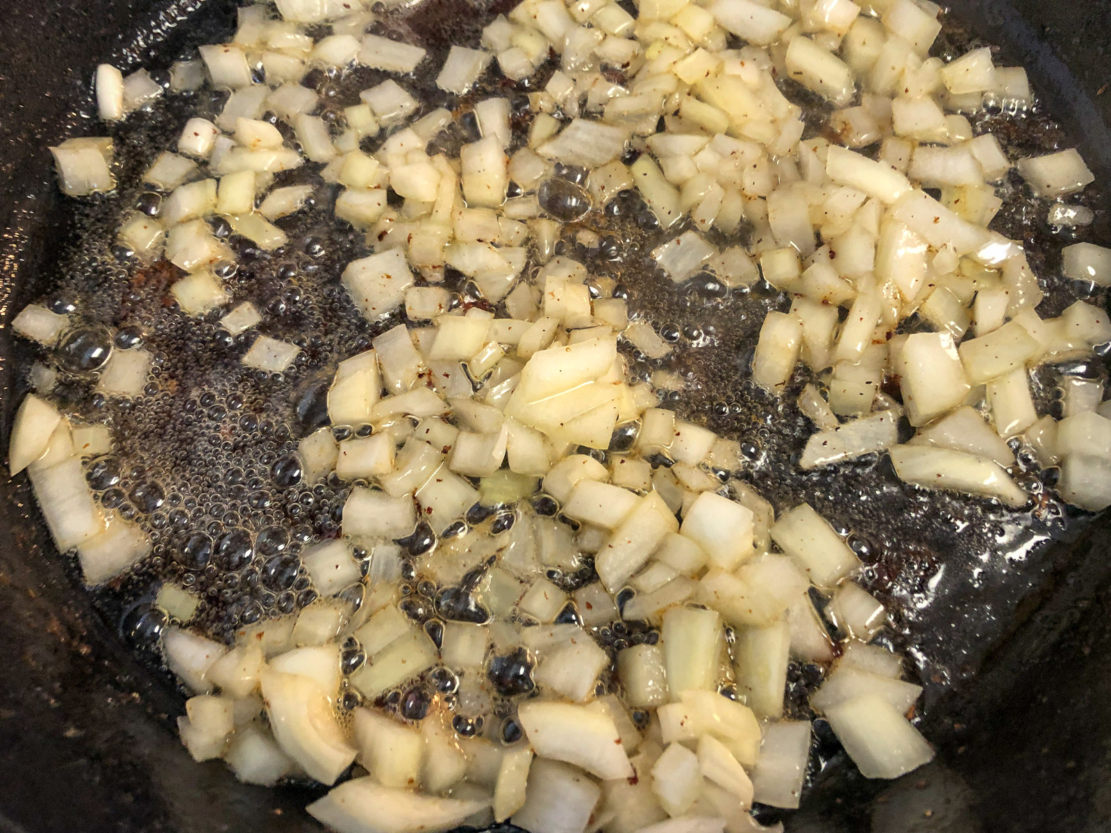 Diced onions sauteing in bacon renderings in a cast iron skillet