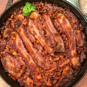 Close up view of southern style baked beans with bacon in a cast iron skillet.