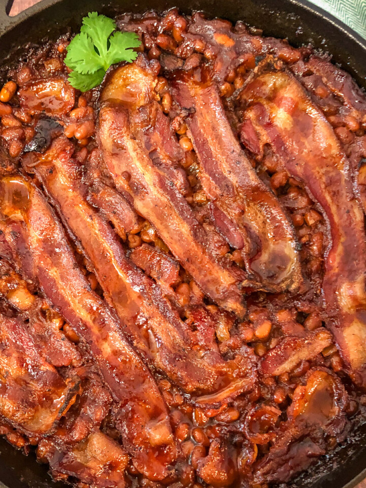 Close up view of southern style baked beans with bacon in a cast iron skillet.