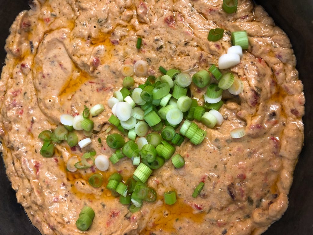 The left over dip and freshly sliced green onions in a cast iron skillet.