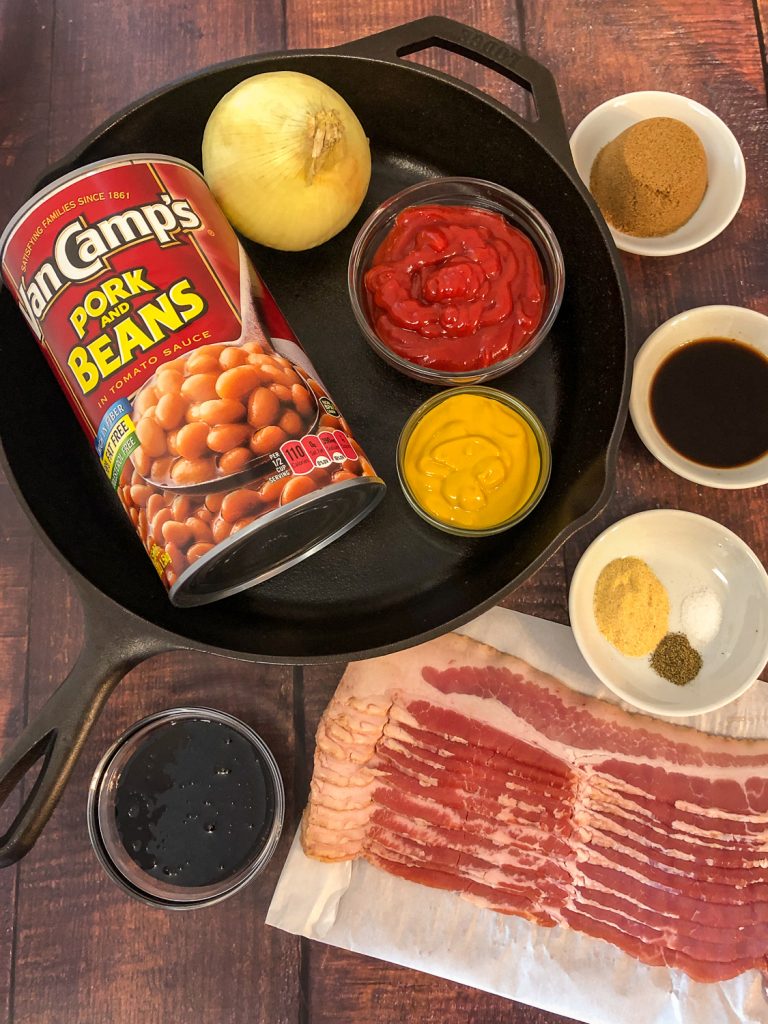 Ingredients to make Southern style baked beans: dark brown sugar, Worcestershire sauce, seasonings, bacon, molasses, pork and beans, onion, ketchup, and mustard with a cast iron skillet.