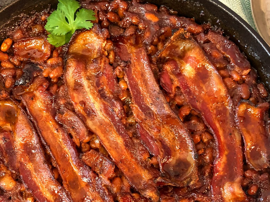 Close up of the cooked southern style baked beans with bacon in the cast iron skillet and a green garnish. 