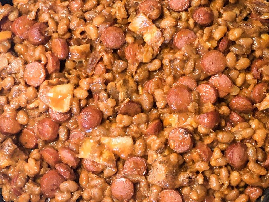 Baked beans with bacon have been added to sliced hot dogs in the skillet.