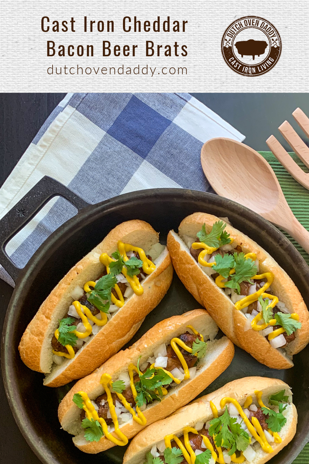 Branded image of the Cast Iron Cheddar Bacon Beer Brats garnished with onions, cilantro, and mustard in the skillet, wooden utensils off to the side. 