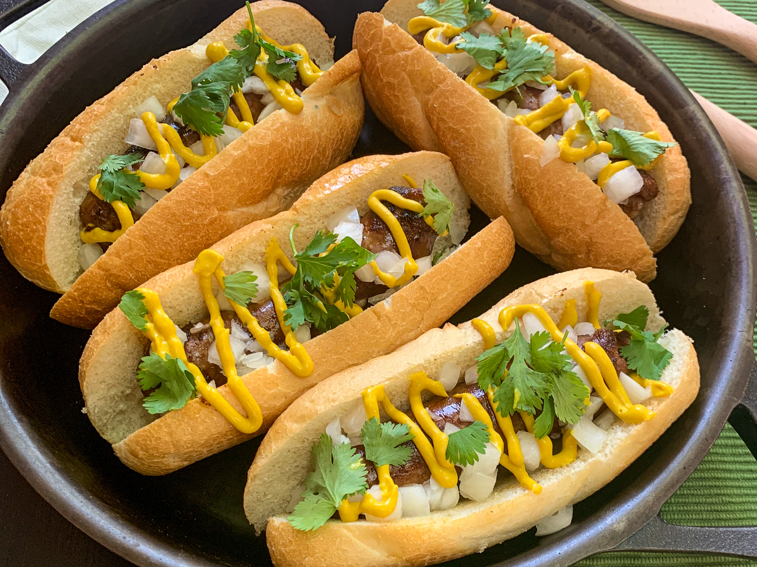 Garnished cheddar bacon beer brats in a skillet.