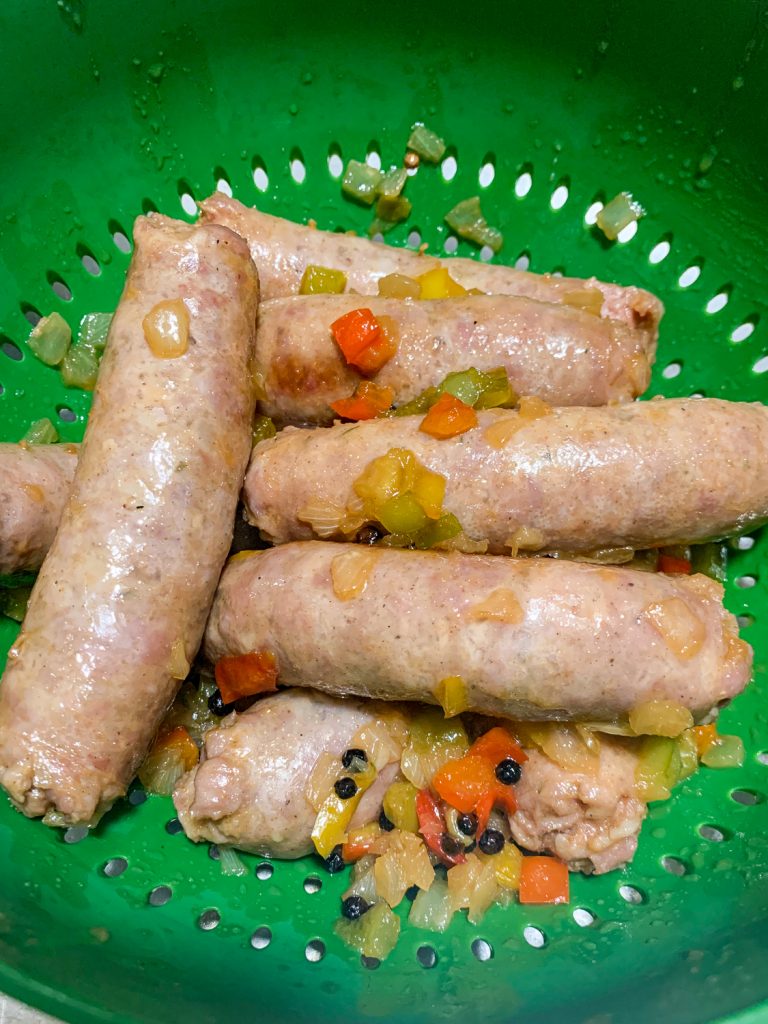 Drained brats after boiling in a green colander. 