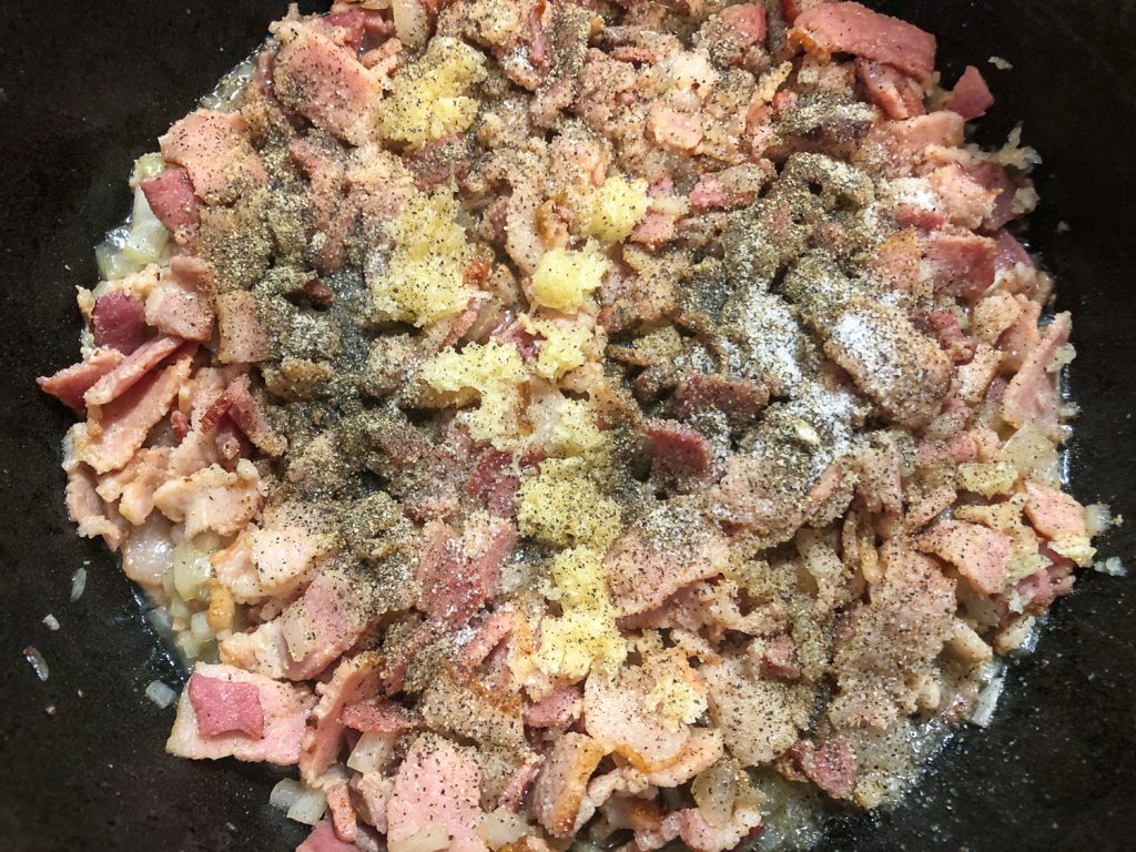 Chopped bacon and onion cooking in a Dutch oven, salt, pepper ,and garlic have been added. 