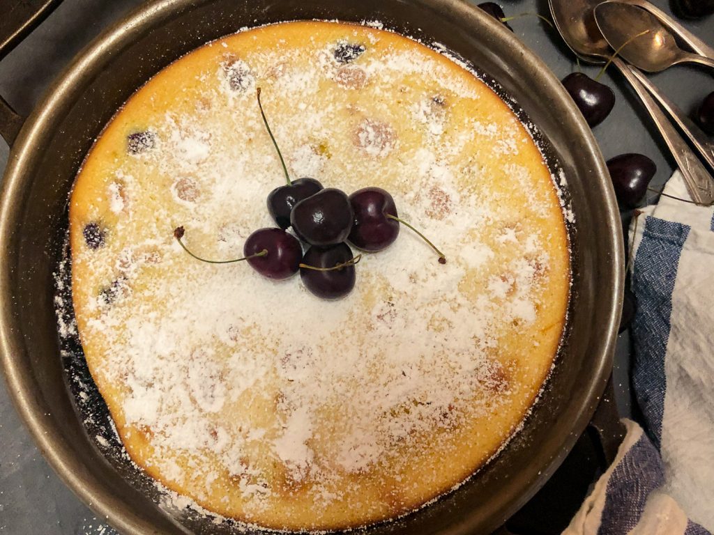 Skillet Cherry Clafoutis fresh from the oven, dusted with powdered sugar and garnished with fresh cherries.