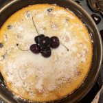 Cherry Clafoutis in a cast iron skillet dusted with powered sugar and garnished with fresh cherries.