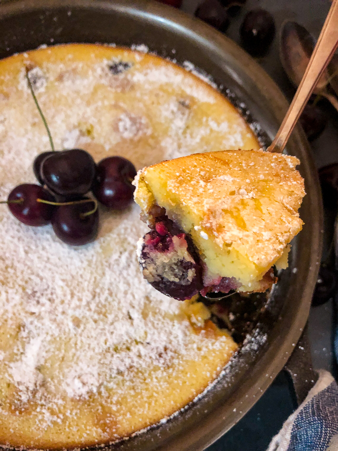 A bite of cherry clafoutis being removed from the skillet. 