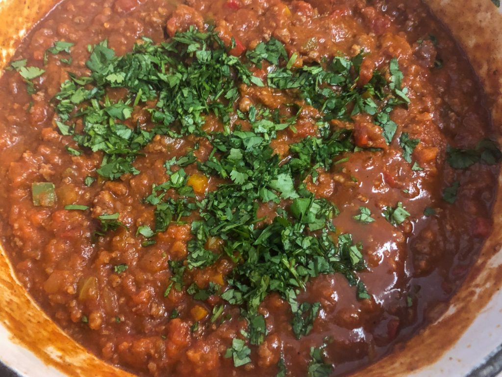 Fresh chopped cilantro has been added to the pumpkin chili in the Dutch oven. 