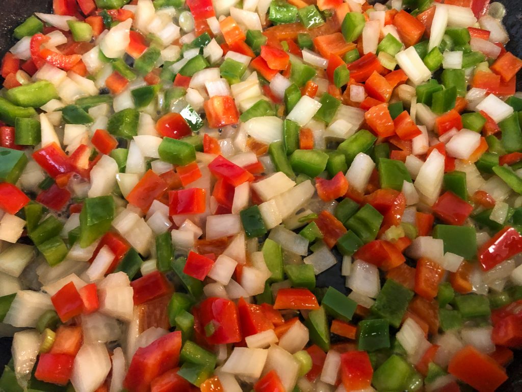 Diced onions and bell peppers sautéing in a cast iron skillet.