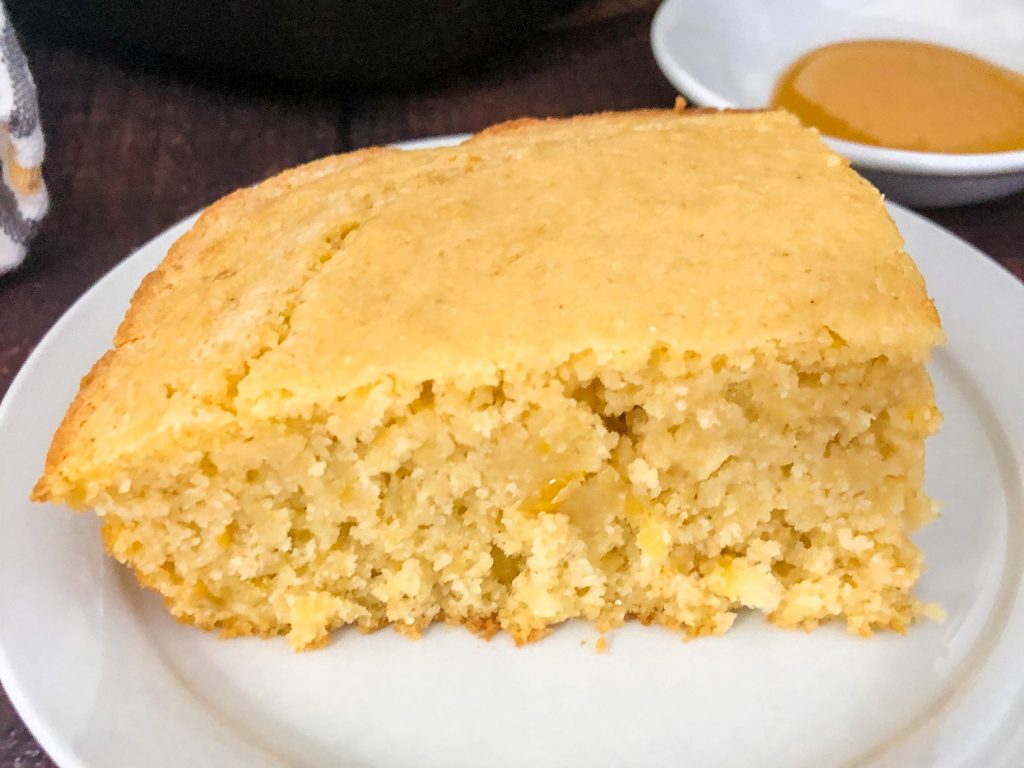 A piece of creamed corn cornbread on a white plate raised to show texture. 