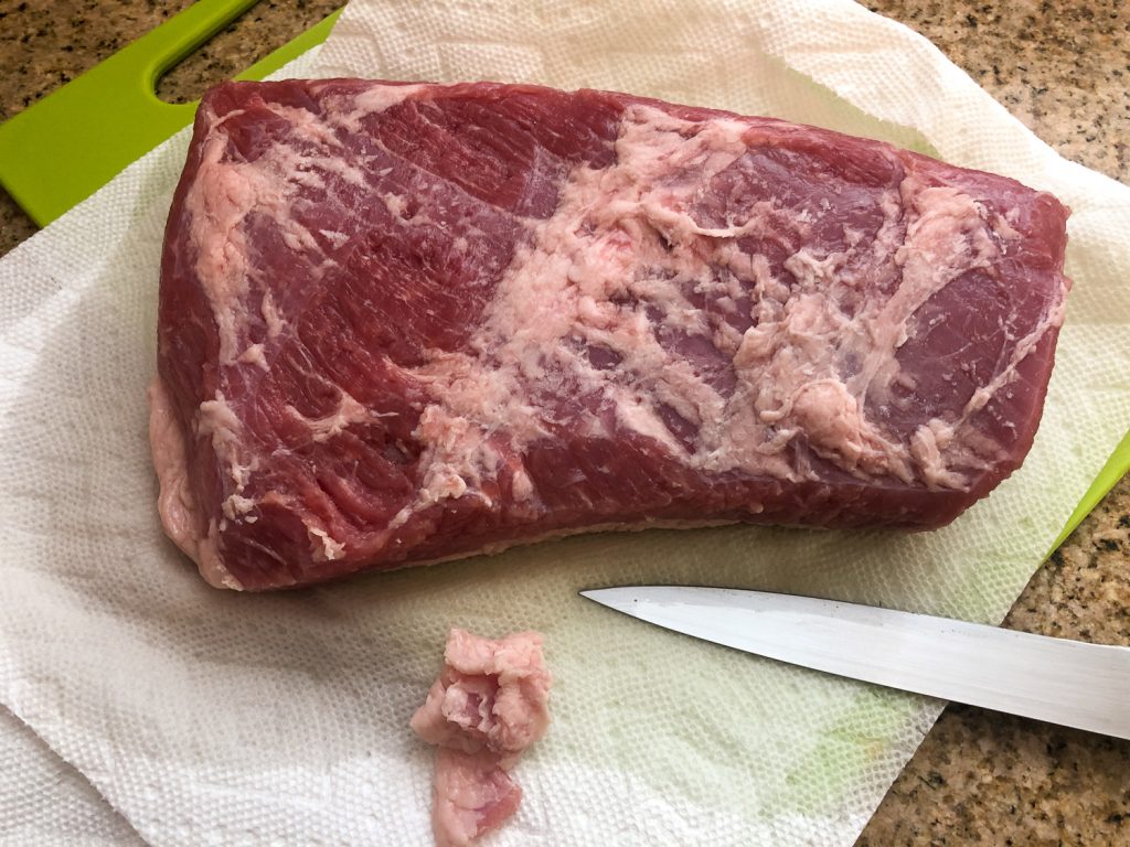 Raw corned beef being trimmed for cooking.