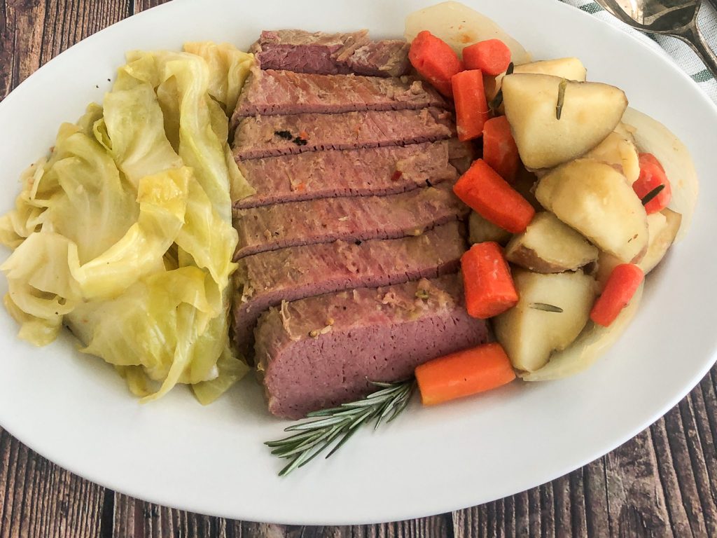 Plated corned beef, cabbage, onions, carrots, and potatoes with a sprig of fresh rosemary. 