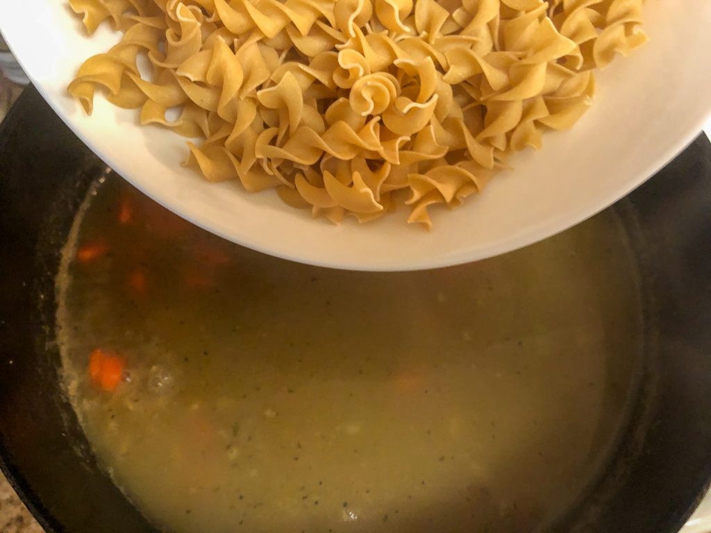 Egg noodles being added to the vegetables and broth in the Dutch oven. 