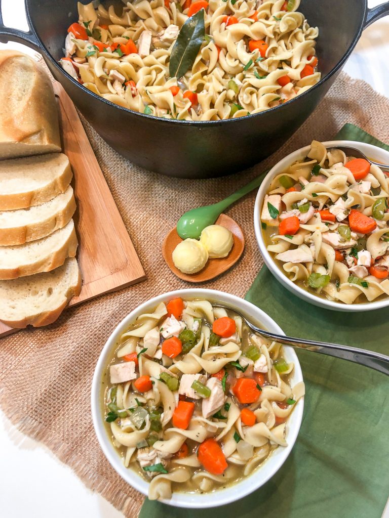 Two bowls of chicken noodle soup, sliced bread, butter, and the dutch oven. 