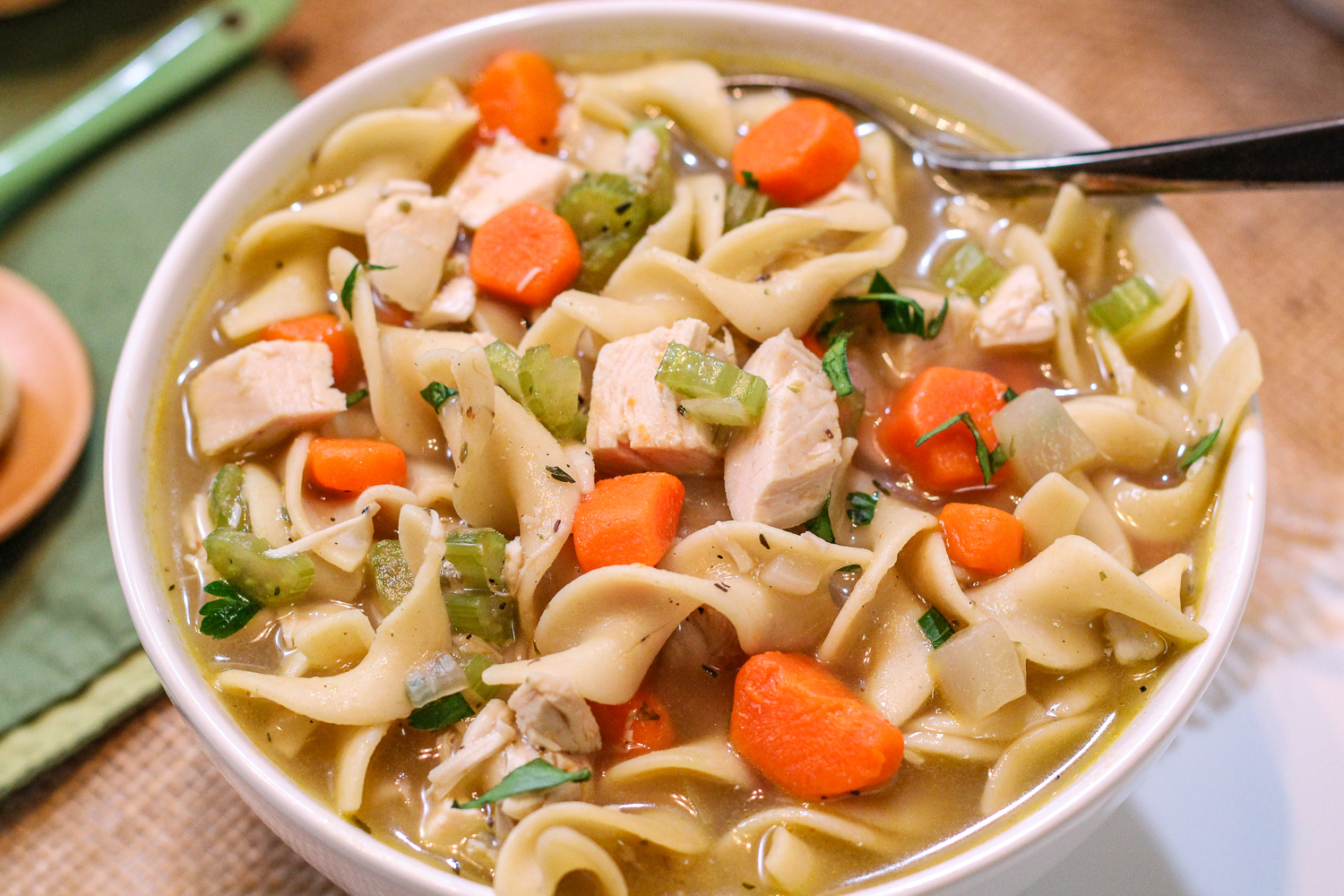 Close up image of chicken noodle soup in a white bowl.