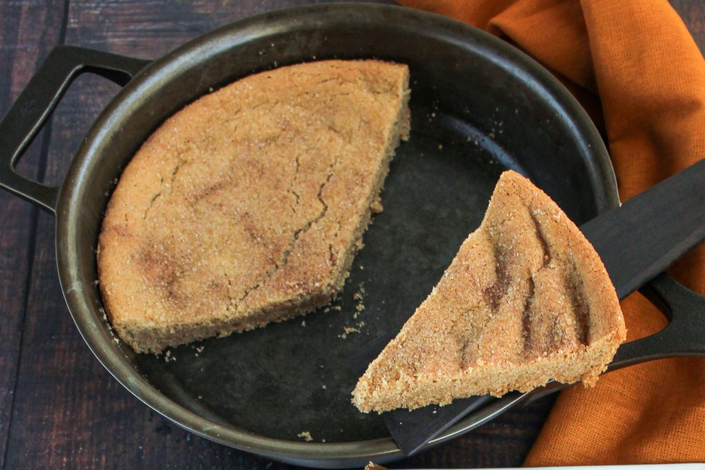 A wedge-slice of cookie raised above the skillet with the remaining cookie inside. 