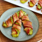 Three bacon wrapped pickles on a plate.