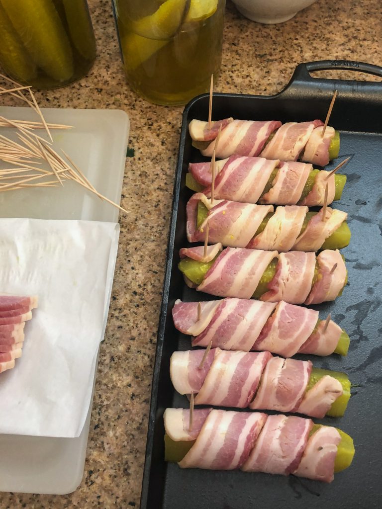 Wrapping strips of bacon around pickles and securing in place with toothpicks.