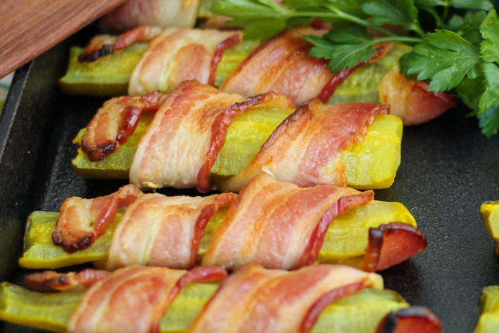 Close up of cooked and crisped bacon wrapped pickles. 