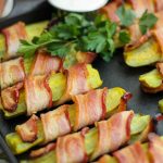Bacon wrapped pickles on the cast iron baking pan garnished with fresh parsley and ranch dip.