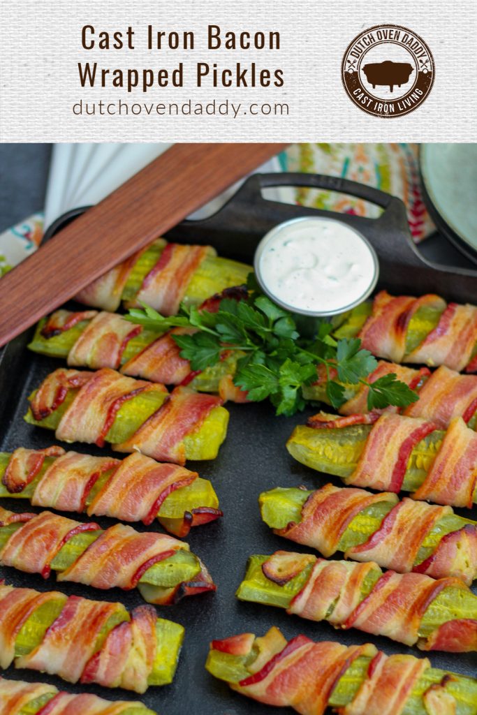 Branded image of bacon wrapped pickles on a cast iron baking pan garnished with fresh parsley and ranch dipping sauce. 