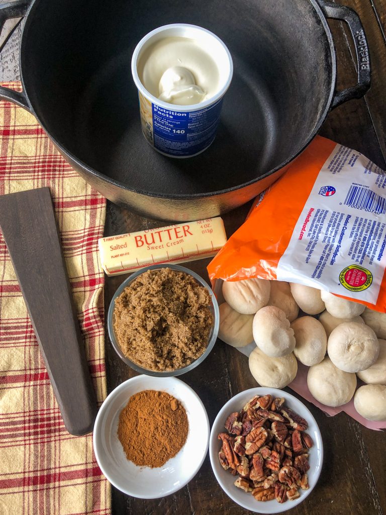 Ingredients to make the recipe: cinnamon, pecans, frozen dinner rolls, brown sugar, butter, prepared cream cheese frosting, and the Dutch oven. 