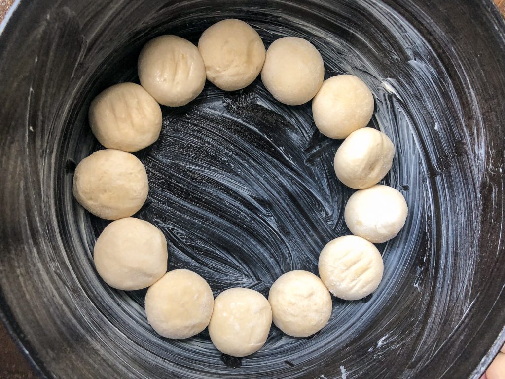 Butter coating the inner surfaces of the Dutch oven and frozen dinner rolls placed inside.