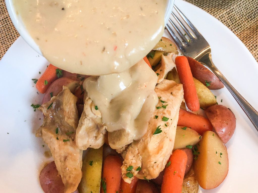 Gravy being poured over the cooked Italian chicken and veggies on a white plate. 