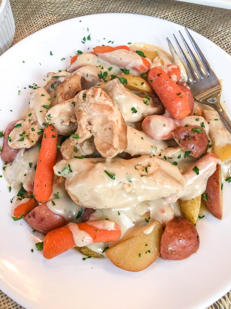Chicken, carrots, and potatoes on a white plate covered in gravy and garnished with fresh parsley. 