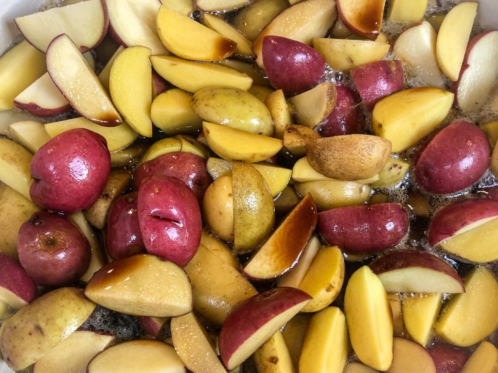 Gold and red baby potatoes have been placed on top of the chicken; the ginger ale and soy sauce have been poured over the top.