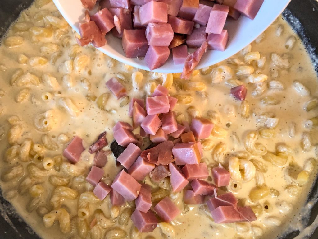 Diced ham being added to the creamy pasta.