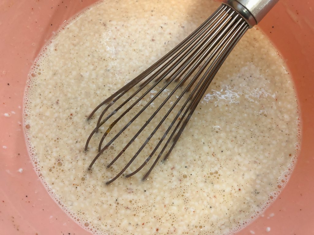 The egg and milk seasoned mixture in a pink bowl with a whisk.