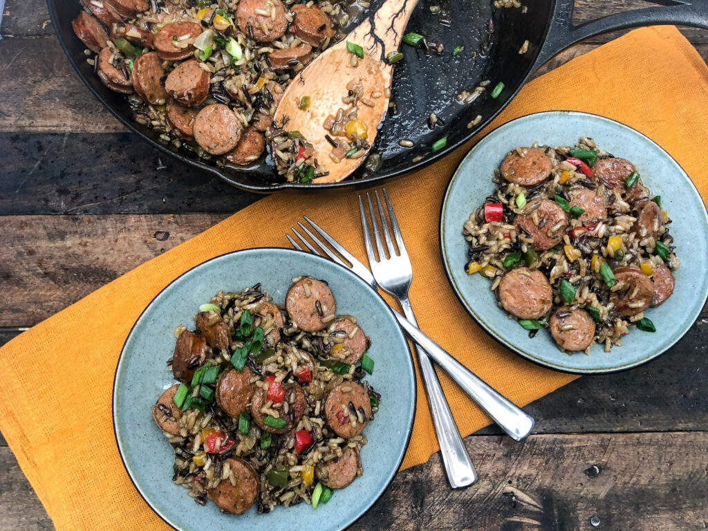 Sausage, Peppers, and Rice plated on two earthen blue plates with forks and the cast iron skillet in the background.