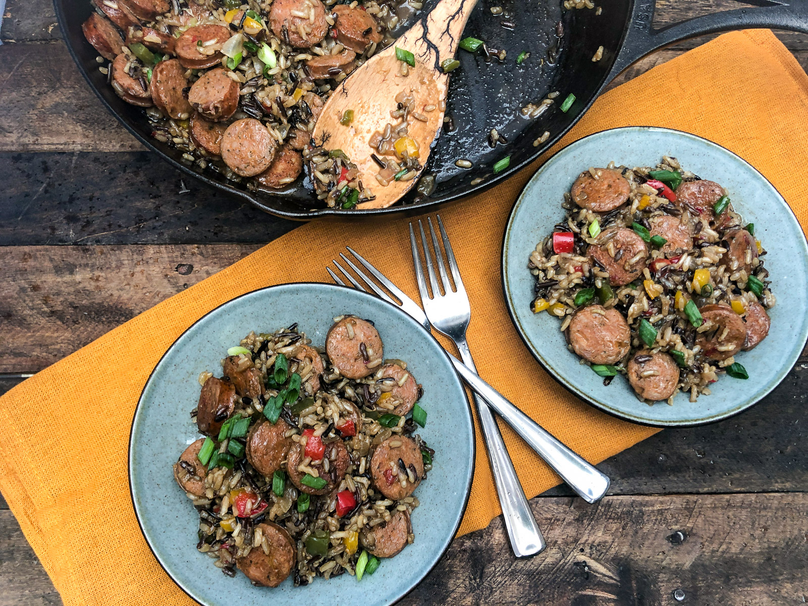 Sausage, Peppers, and Rice plated on two earthen blue plates with forks and the cast iron skillet in the background.