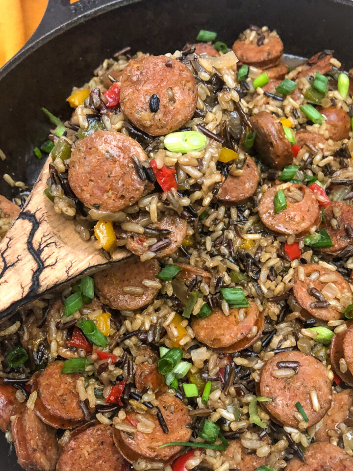 Sausage Peppers and Rice in a cast iron skillet with a wooden serving spoon.