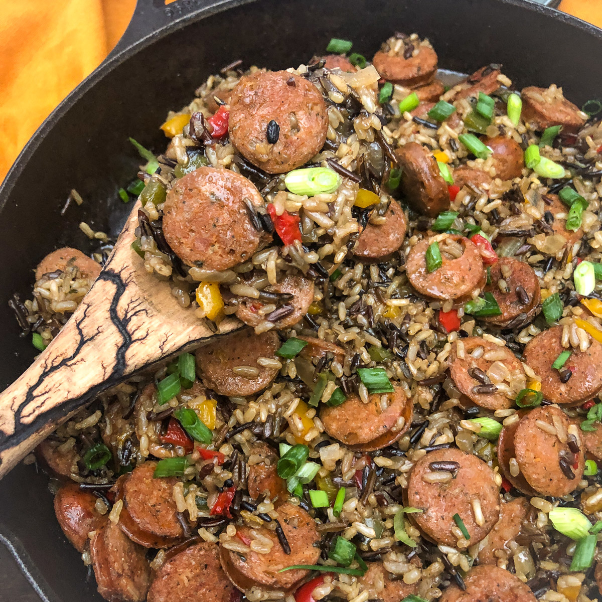 Sausage Peppers and Rice in a cast iron skillet with a wooden serving spoon.