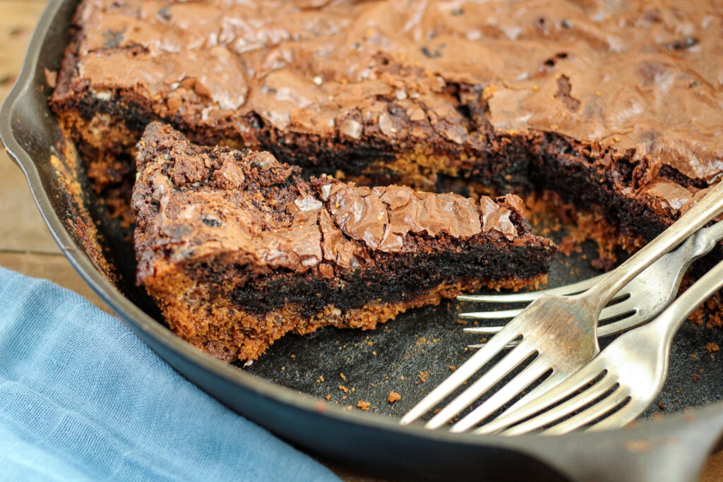 A pie-shaped piece of the brookie in the cast iron skillet with several forks.