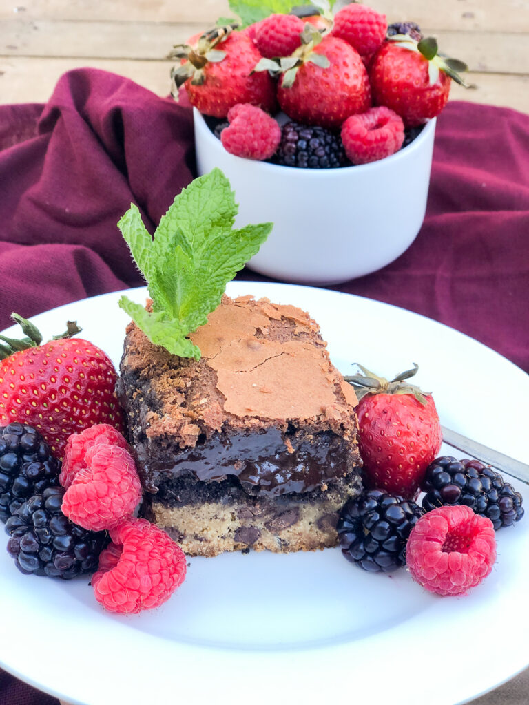 A square piece of Chocolate Chip Cookie Brownie on a white plate garnished with fresh mint and berries.