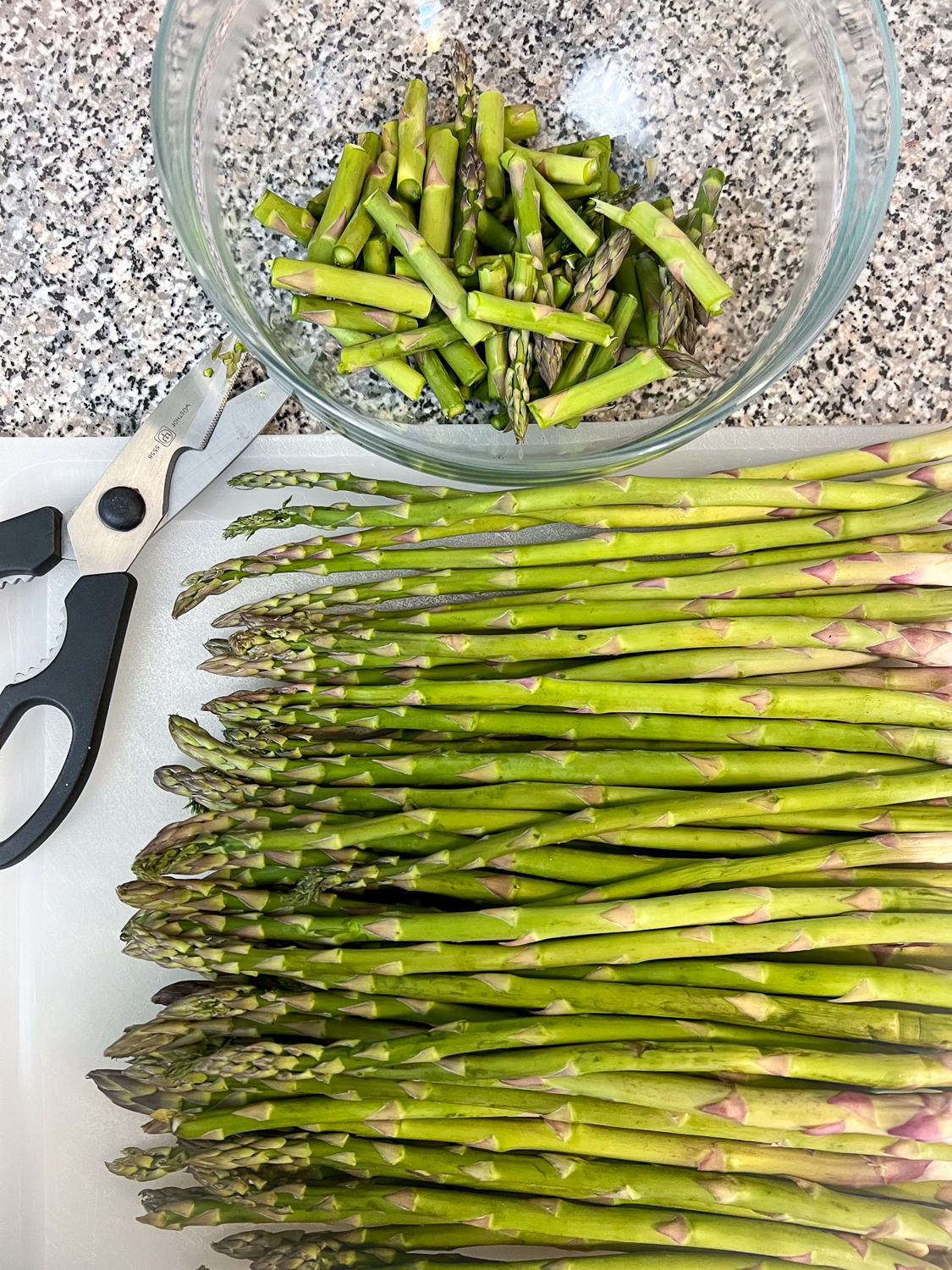 Asparagus being trimmed on a cutting board.